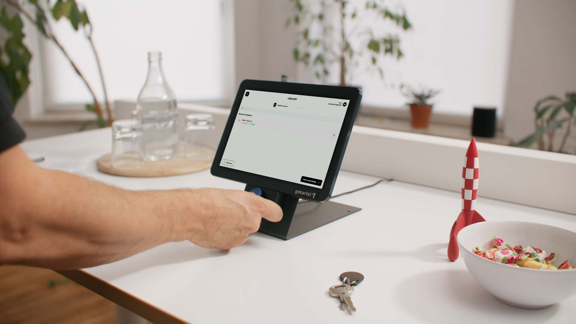 Eine Hand hält einen NFC-Tag an das Log+Key Terminal, am Bildschirm die Liste der gescannten Objekte